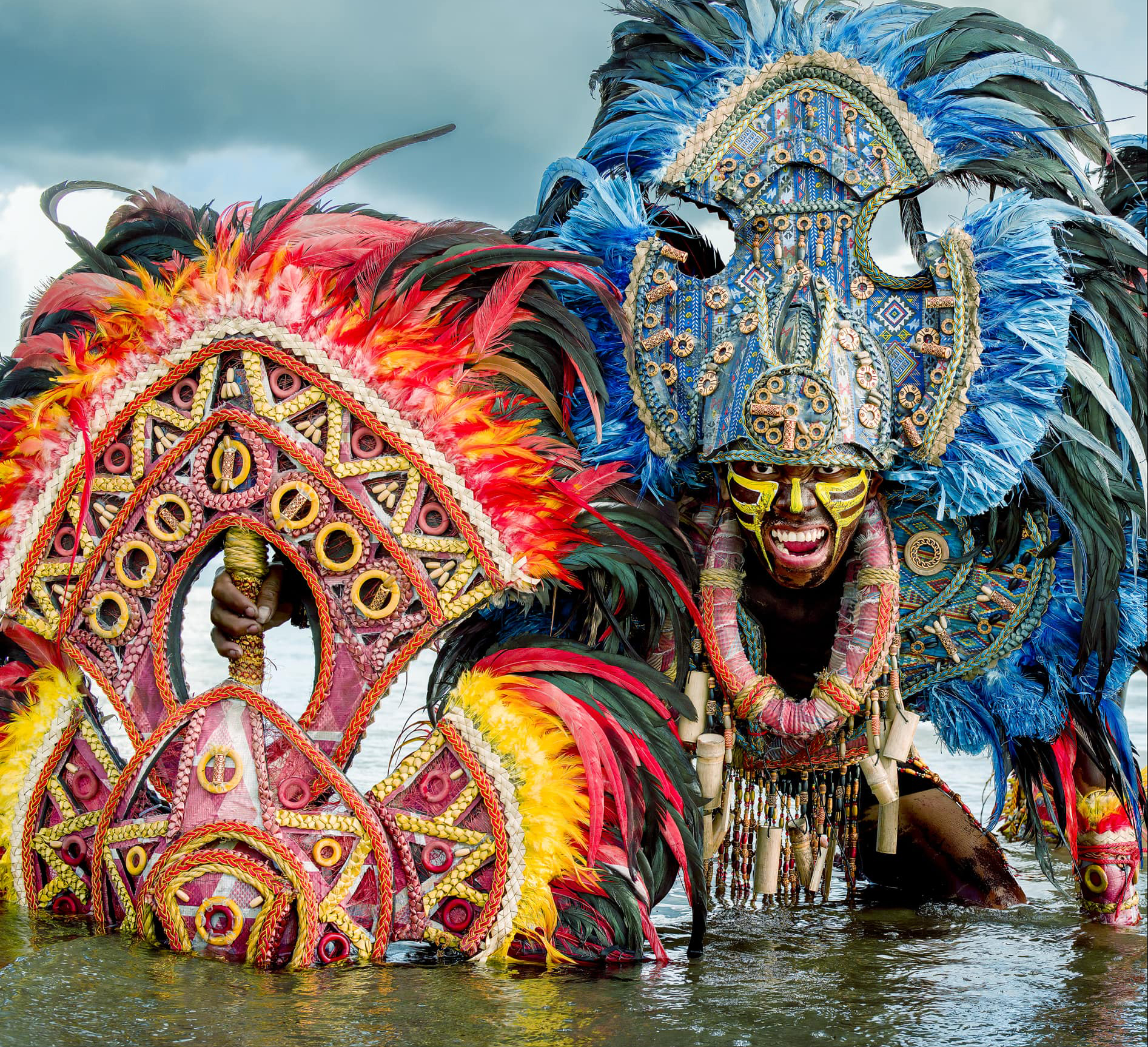 Ati-Atihan warrior in elaborate blue feather headdress kneeling in river water, Aklan, Philippines