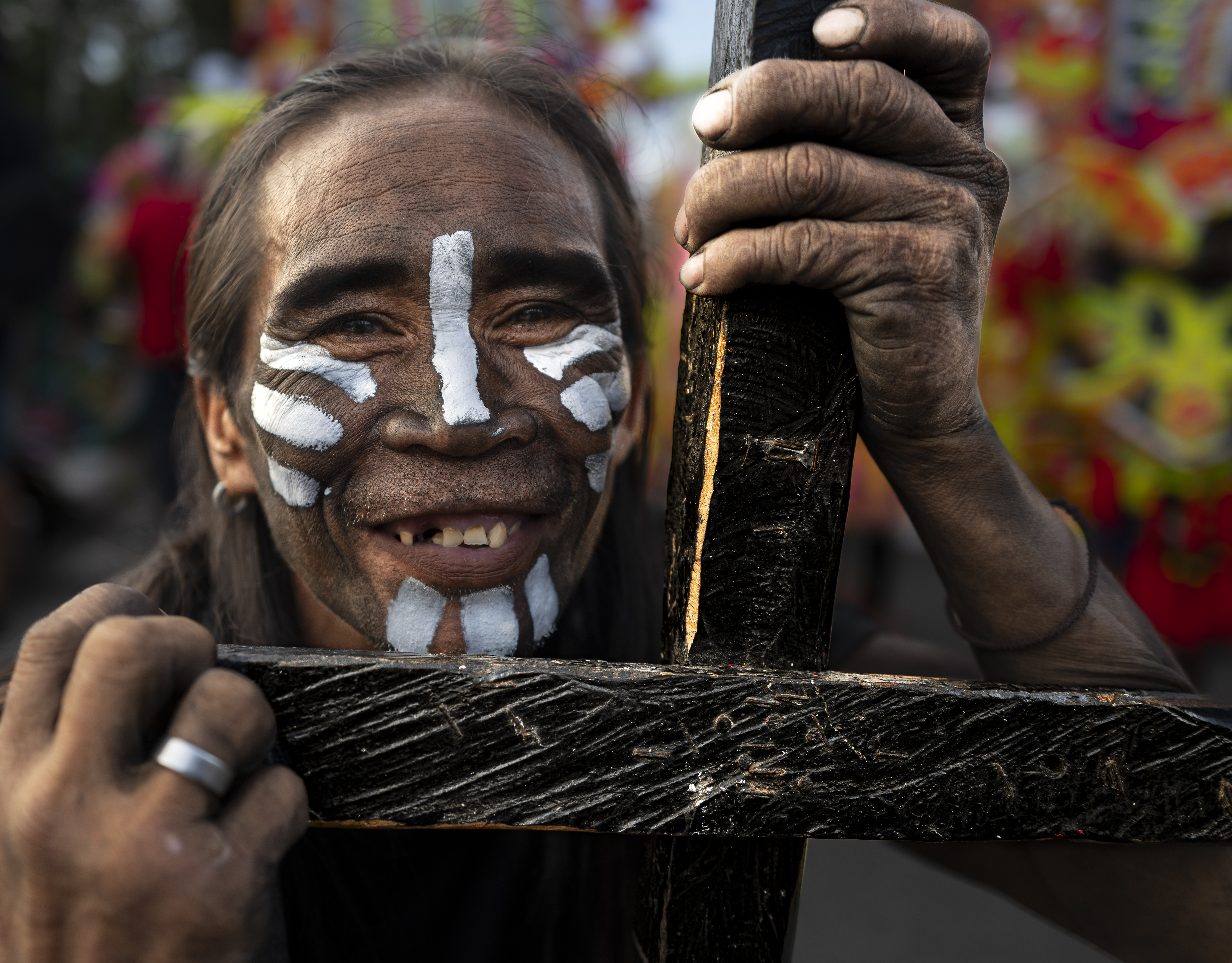 Man with white cross face paint smiling, holding a wooden cross at Ati-Atihan festival, Kalibo, Philippines